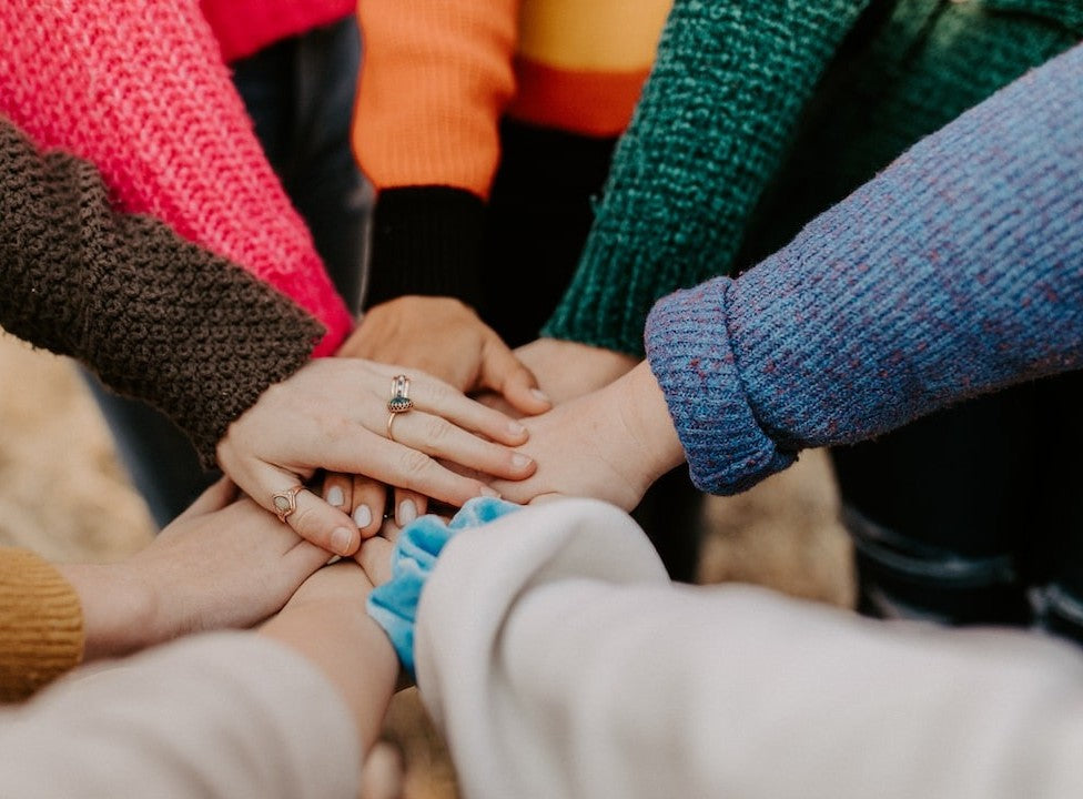 A circle of friends all coming together in the middle with their arms to show support for those with Cancer